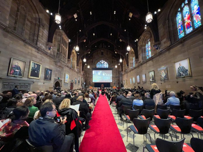 Photo by Andy Wang a group of people sitting in a room with a large screen